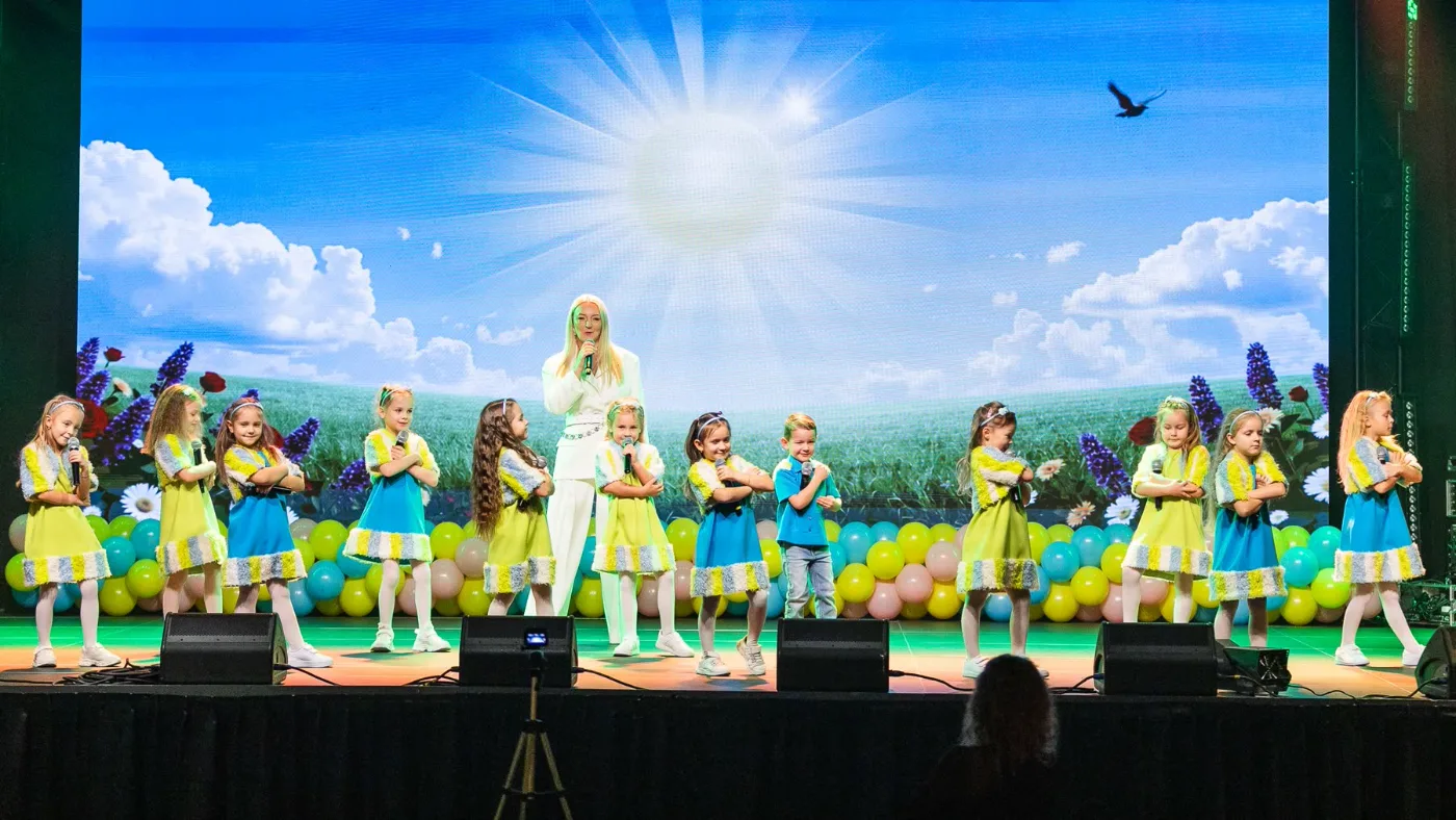 Vaikai su mokytoja dainuoja scenoje